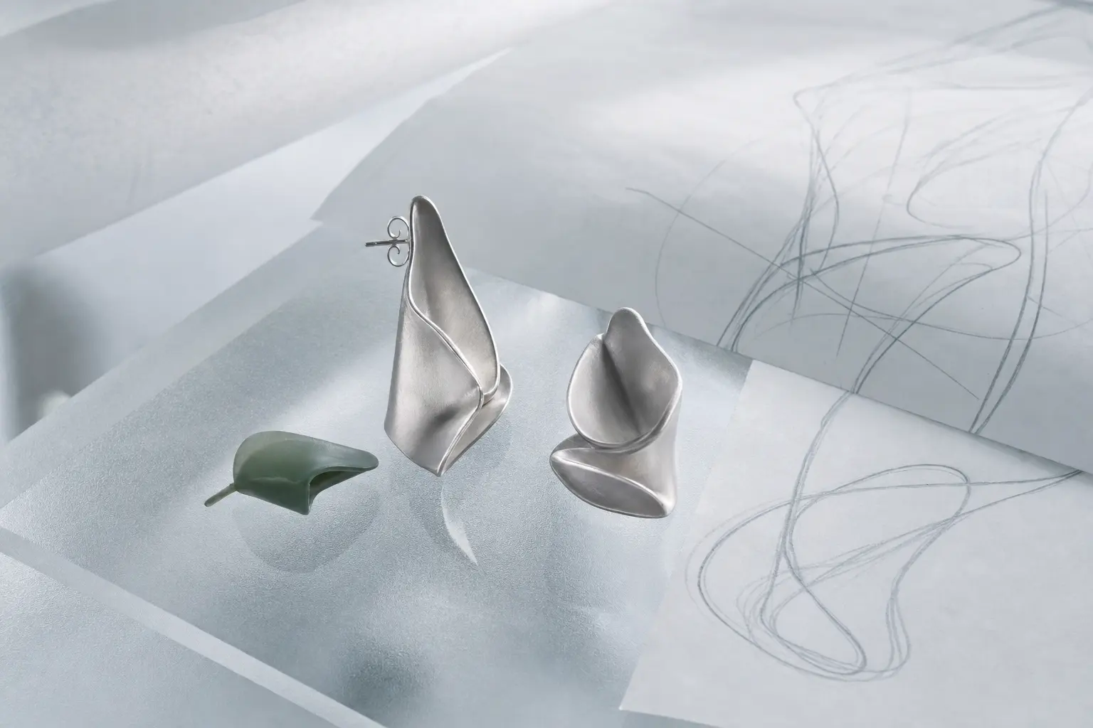 Silver petal earring prototype with soft construction curves on gray film