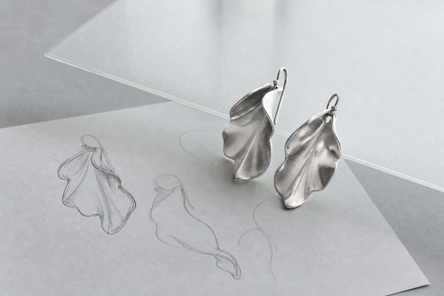 Abstract leaf-like silver earring prototypes over translucent gray paper