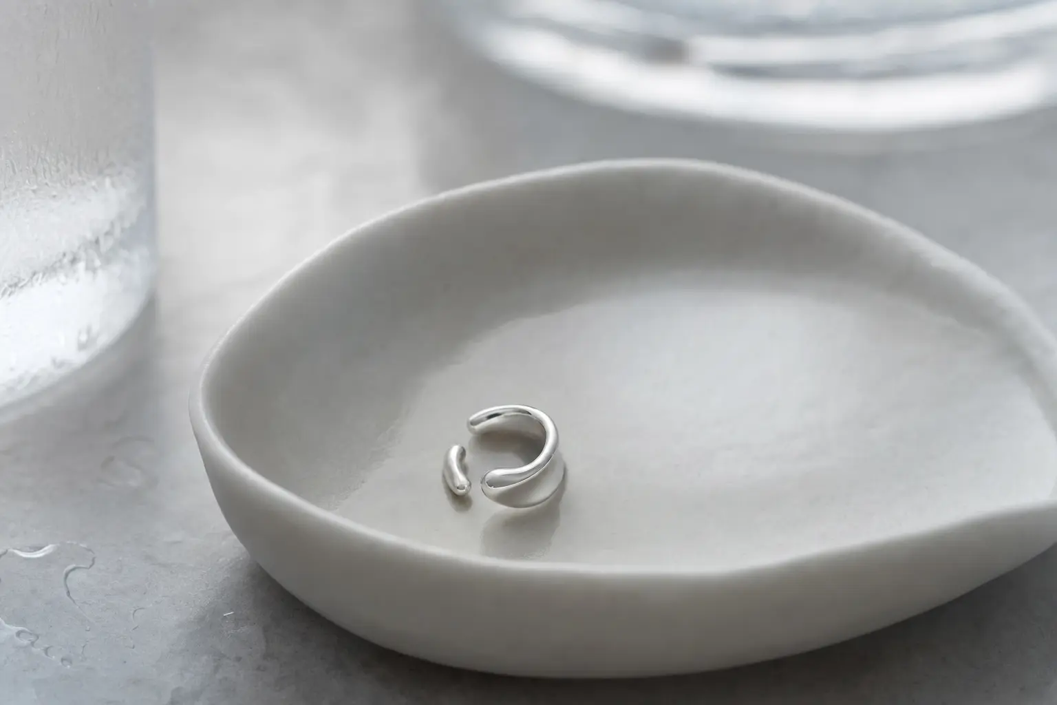 Minimal silver ear cuff resting in a cool gray ceramic dish