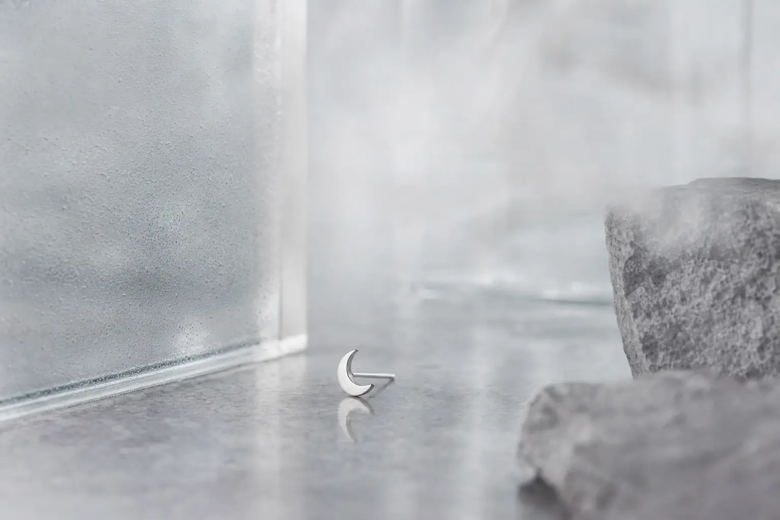 Tiny crescent silver earring detail on misted glass and gray stone