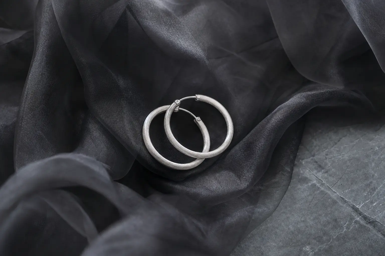 Frosted silver hoop earrings nested in smoky gray fabric folds