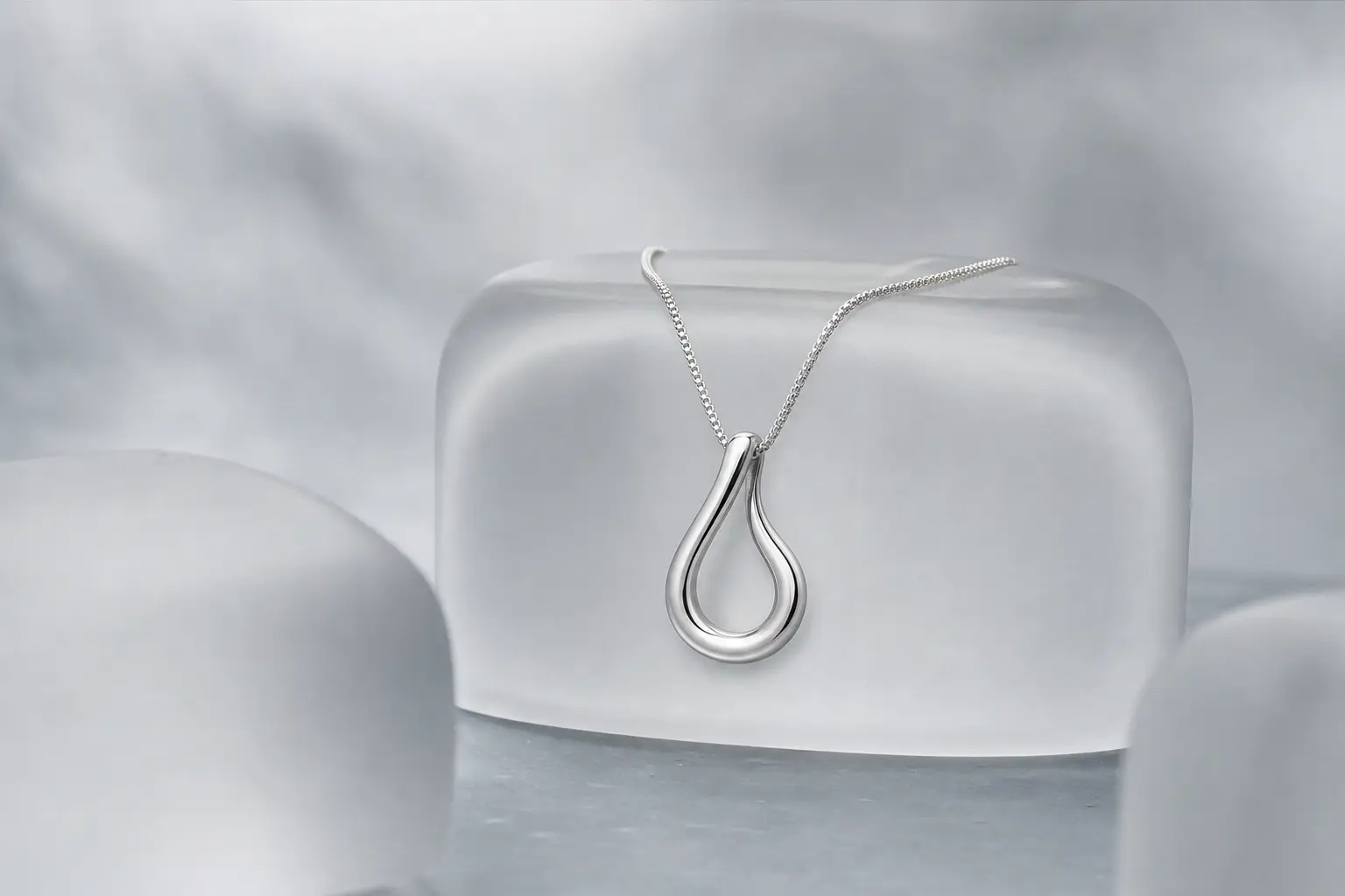 Minimal silver pendant displayed on a rounded frosted acrylic block