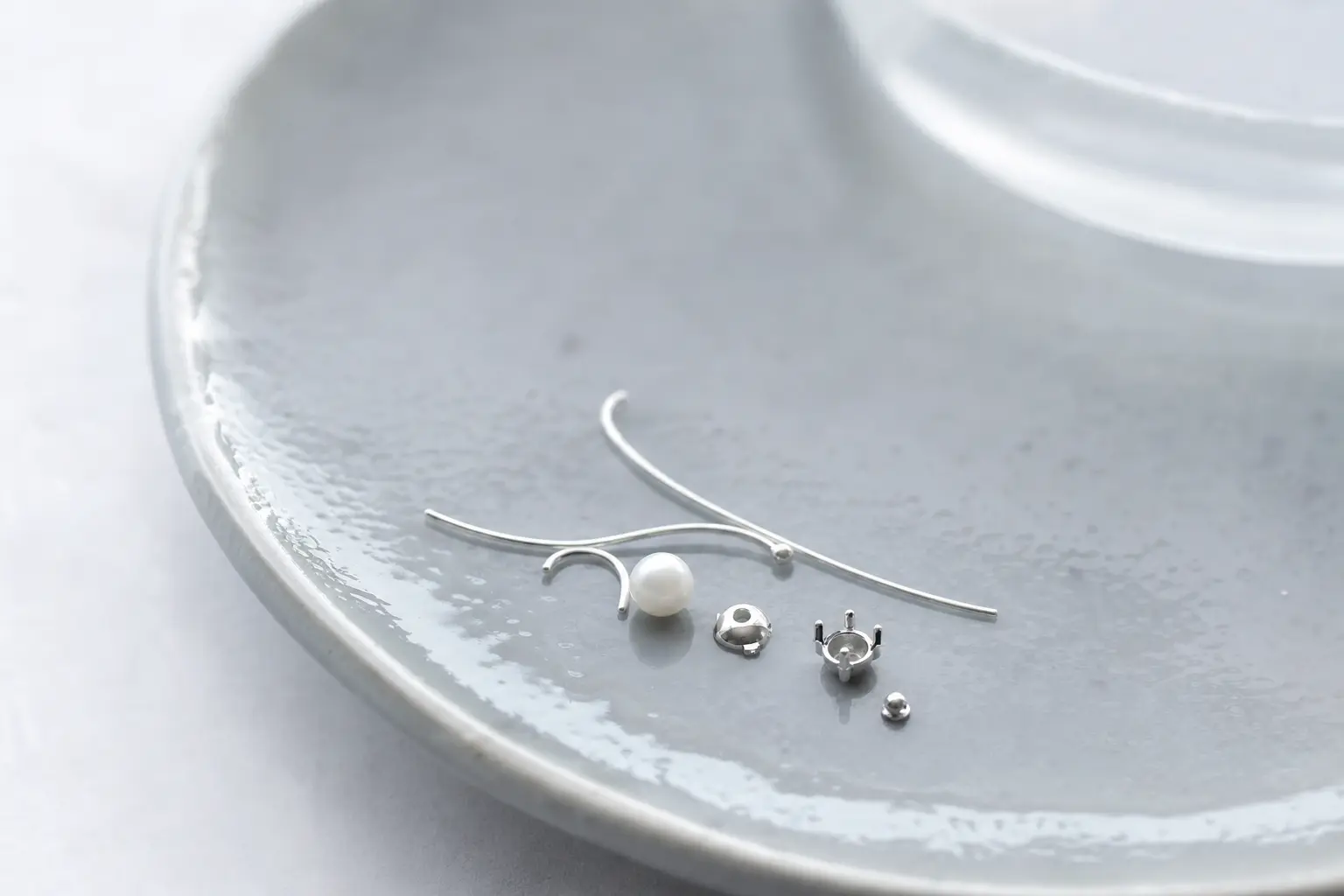Tiny silver wire arcs and pearl-like components on cool gray ceramic