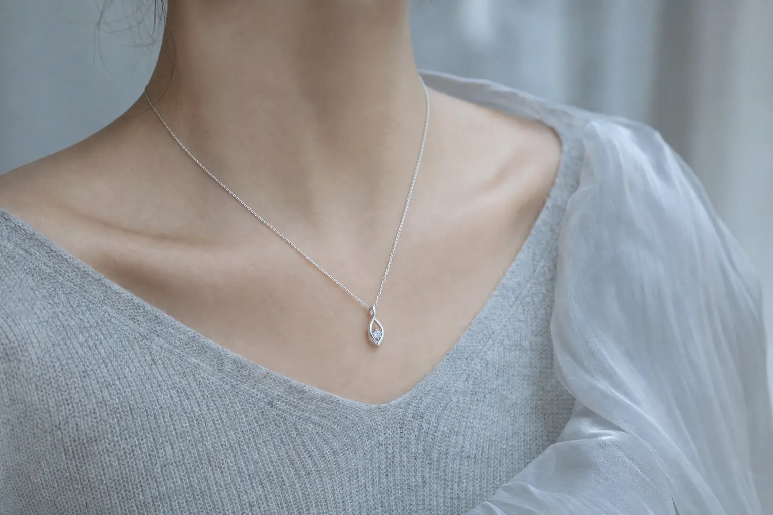 Silver pendant necklace worn with a soft cool gray knit neckline