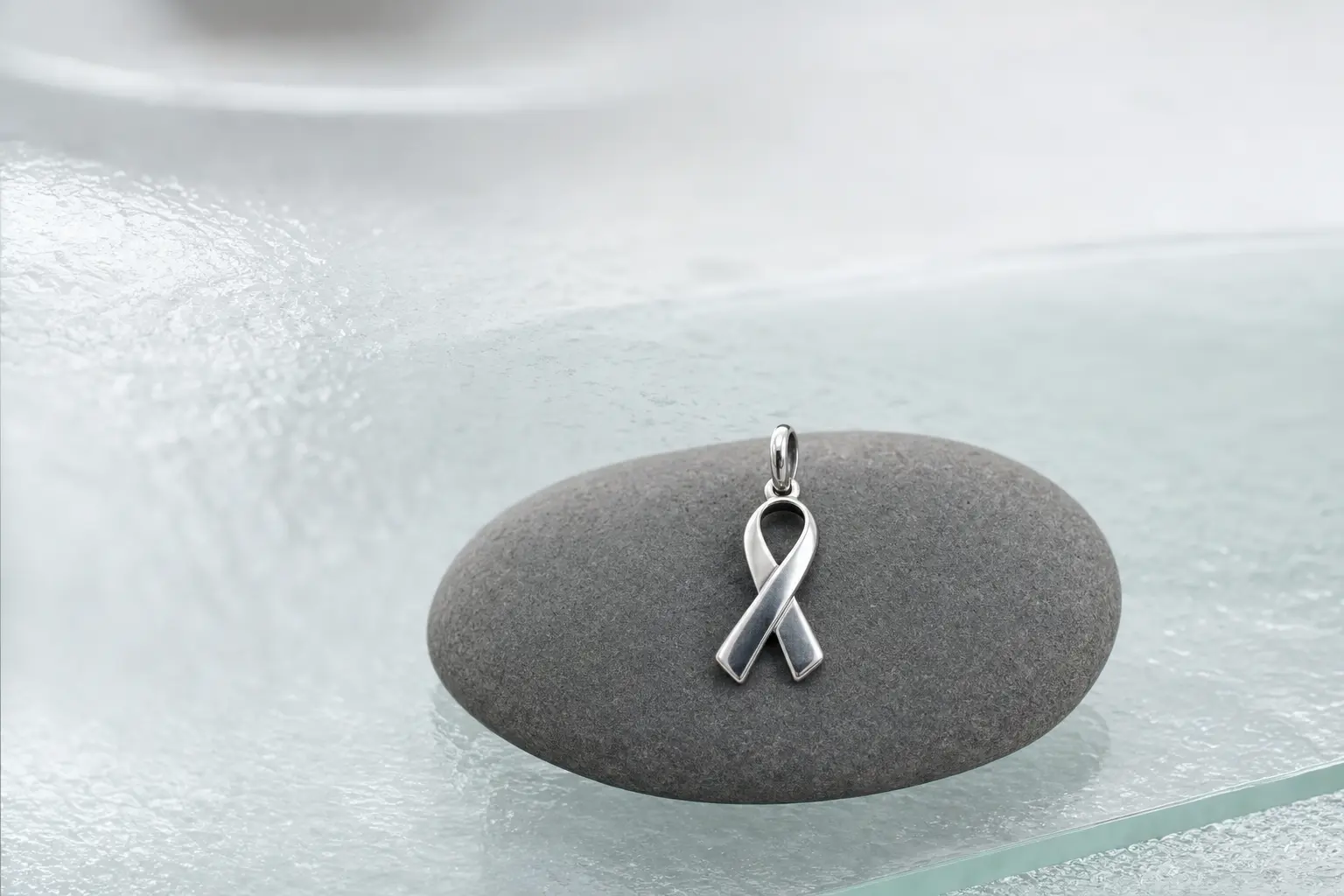 Small silver ribbon pendant on a smooth graphite-gray pebble