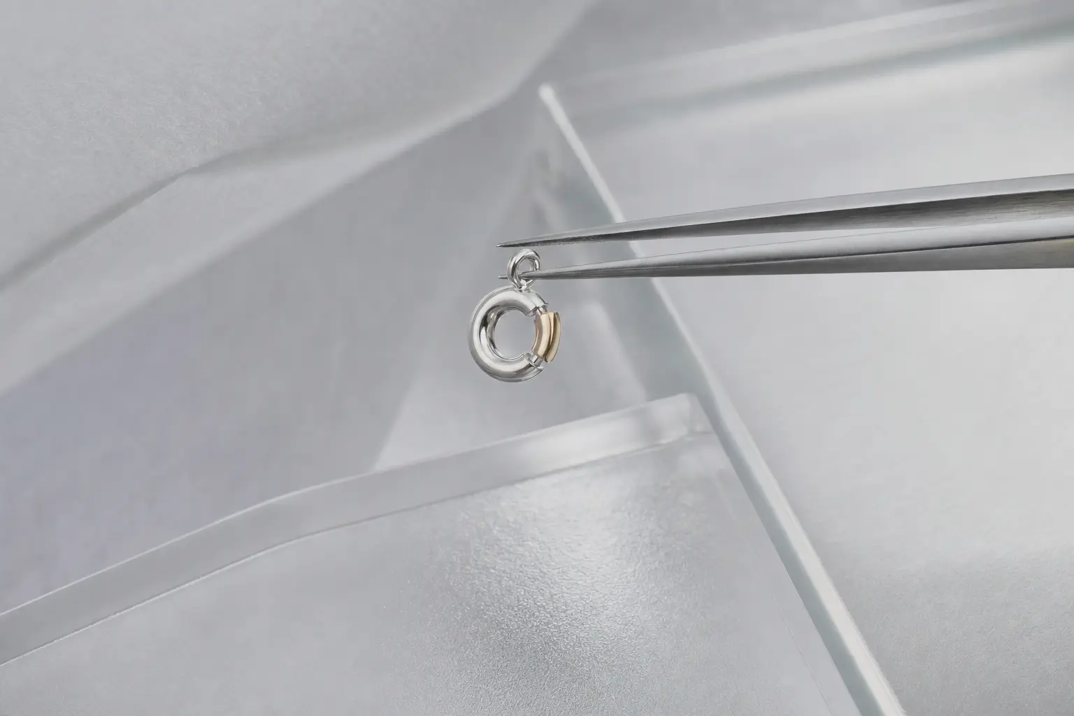 Fine tweezers holding a tiny silver and champagne clasp sample