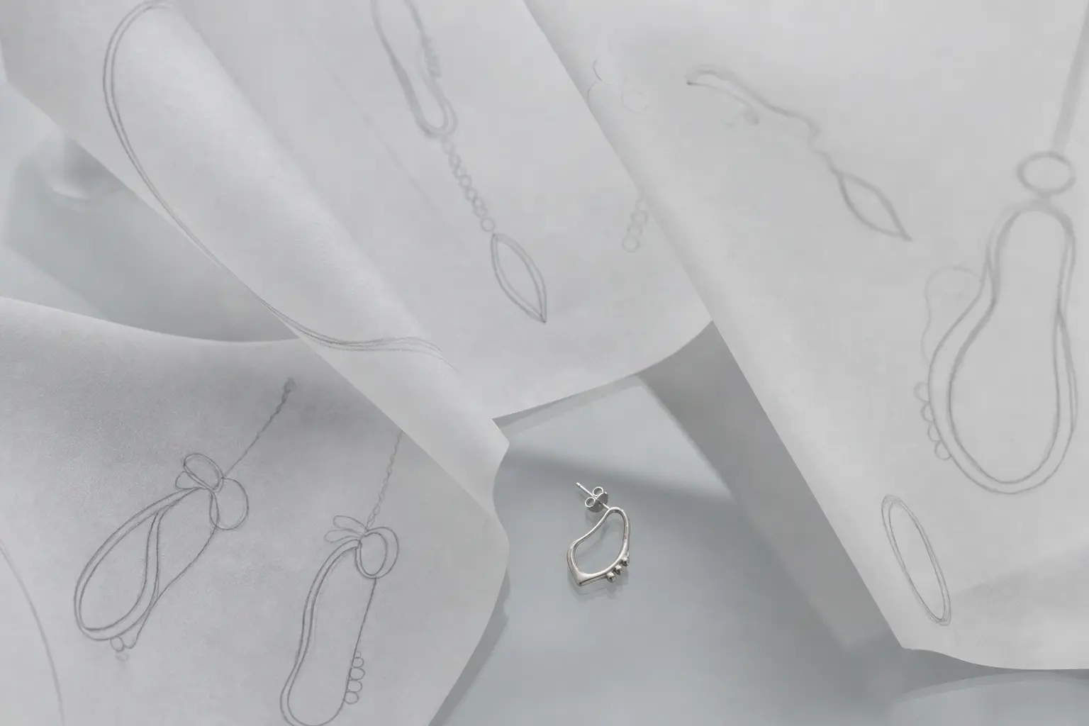 Layered cool gray vellum sketches with a tiny silver prototype