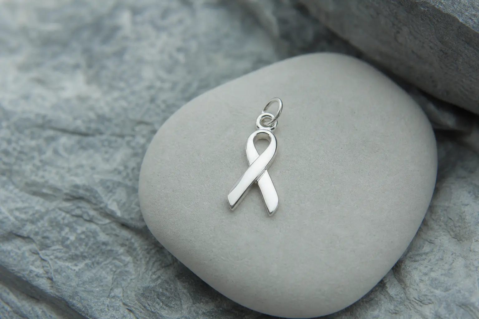 Small polished silver ribbon pendant charm on a pale smooth stone