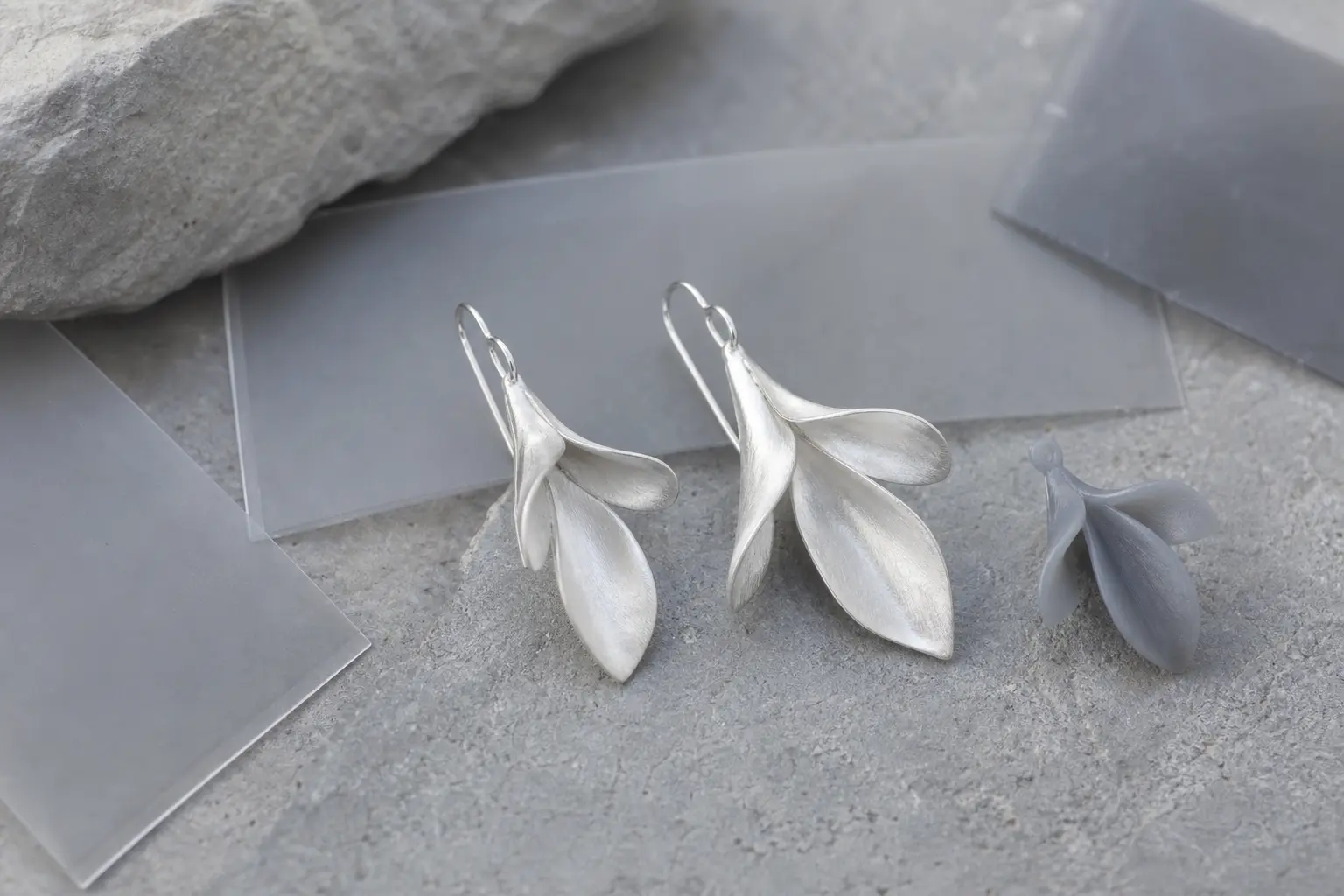 Botanical silver earring prototypes beside translucent film sheets