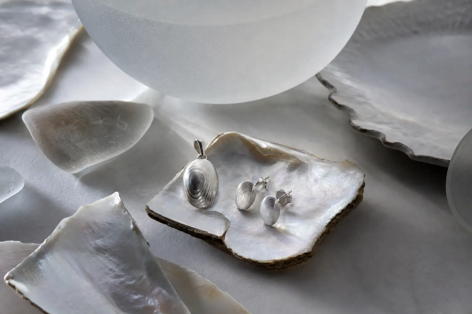 Silver pendant and earrings arranged on mother-of-pearl fragments