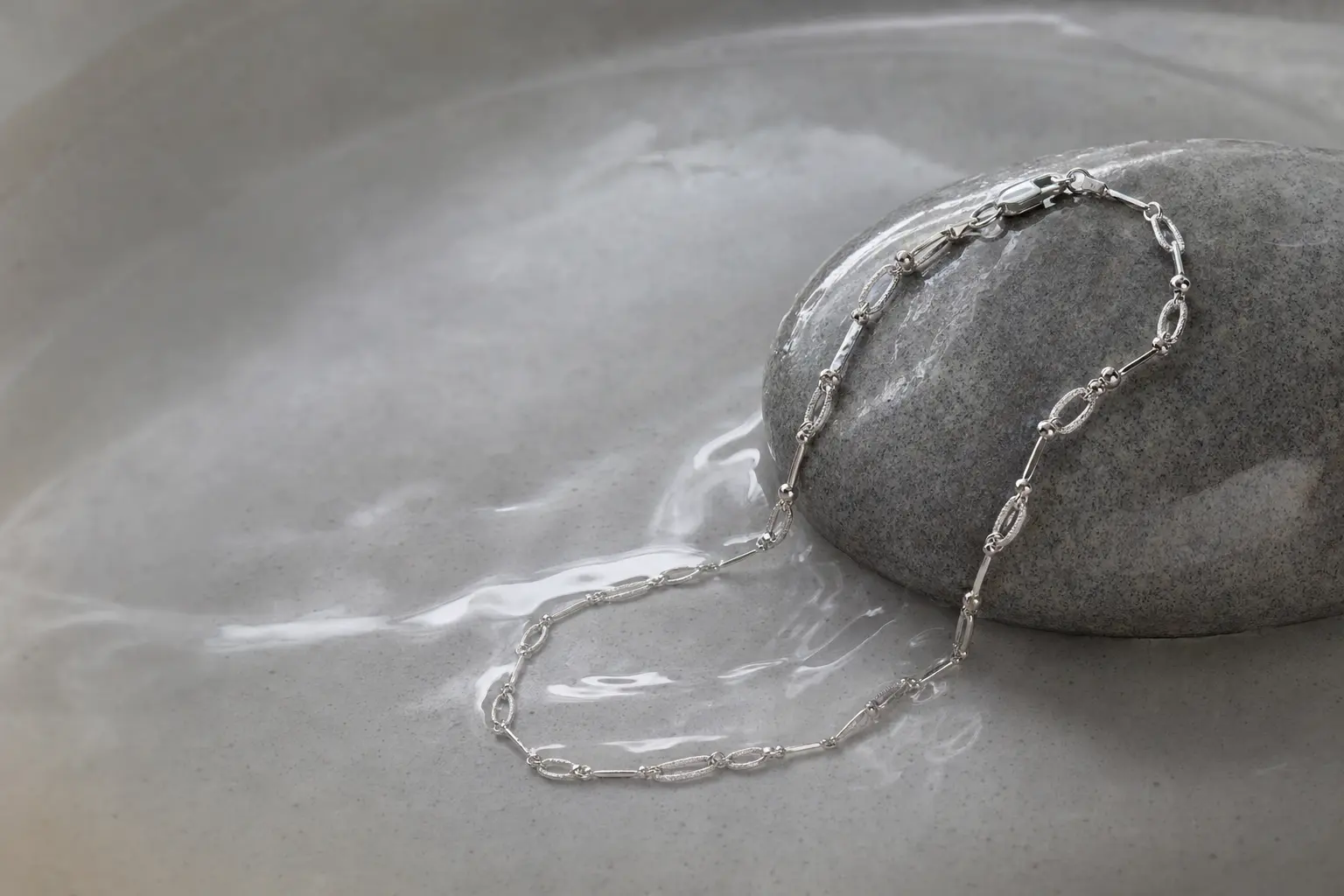 Silver chain bracelet on smooth stone and shallow water