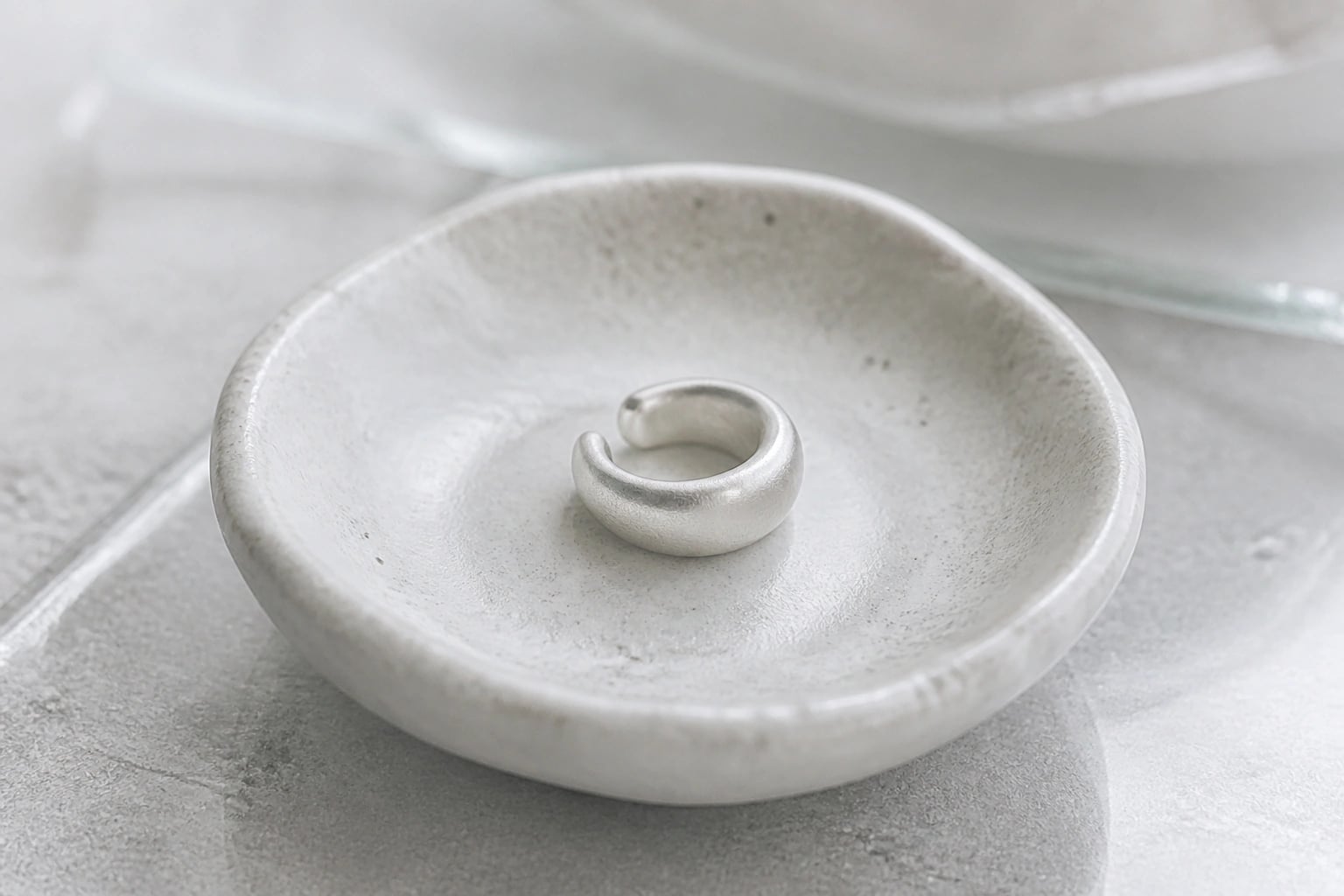 Single satin silver ear cuff resting in a handmade ceramic dish