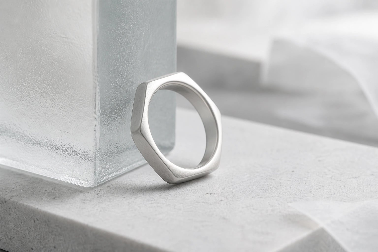 Single satin silver hexagon ring leaning against a frosted glass block