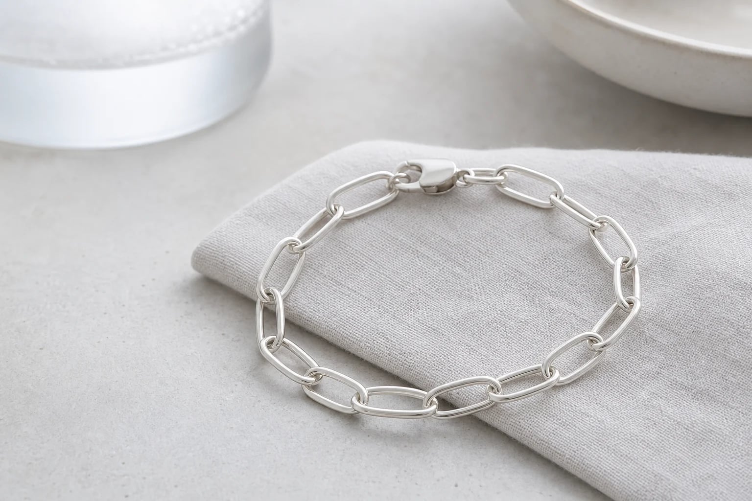 Silver paperclip chain bracelet draped over a soft linen fold