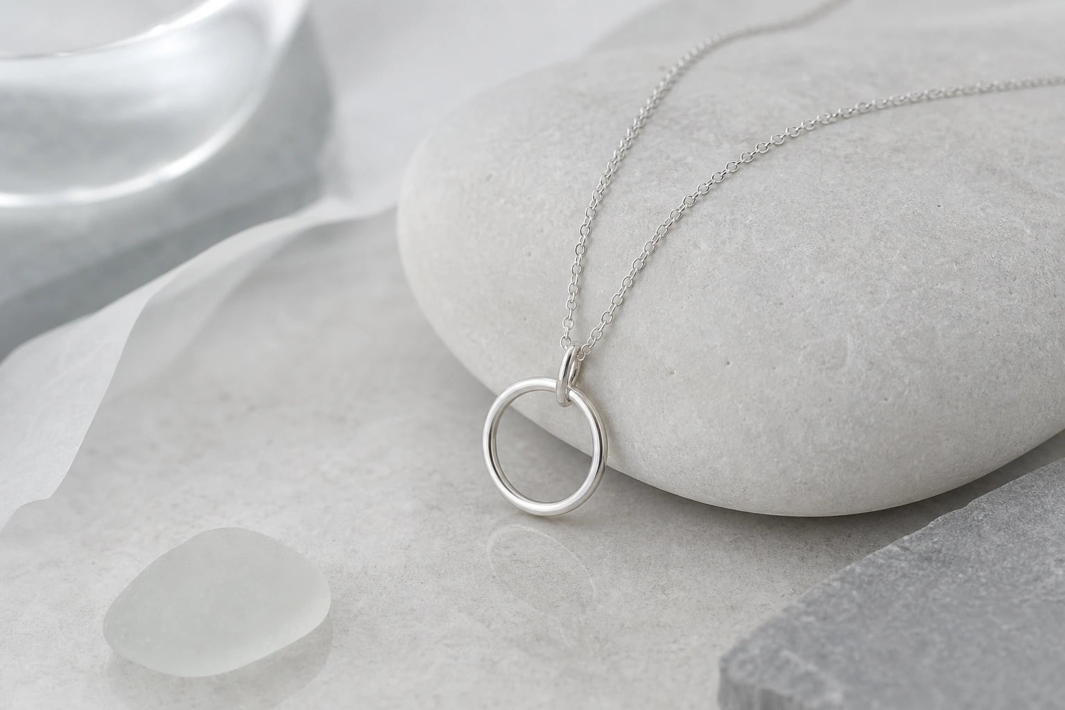 Fine silver necklace with a small open circle pendant draped over a white pebble