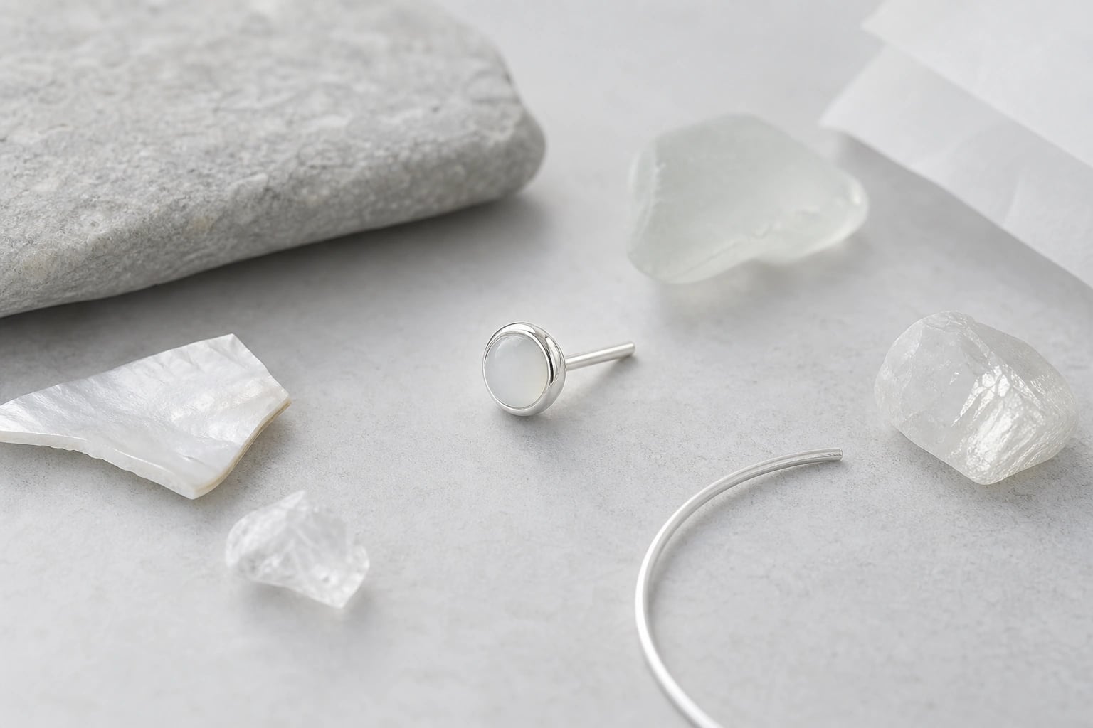 Milky cabochon silver stud among mother-of-pearl, sea glass, and a silver wire arc
