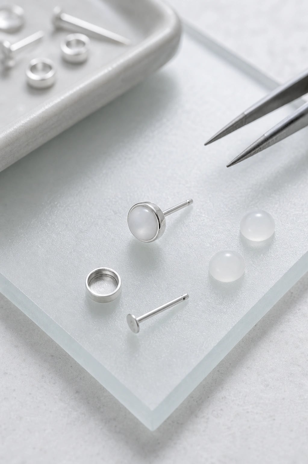 Bezel cup, post, and milky cabochons laid out as a stud assembly on frosted glass