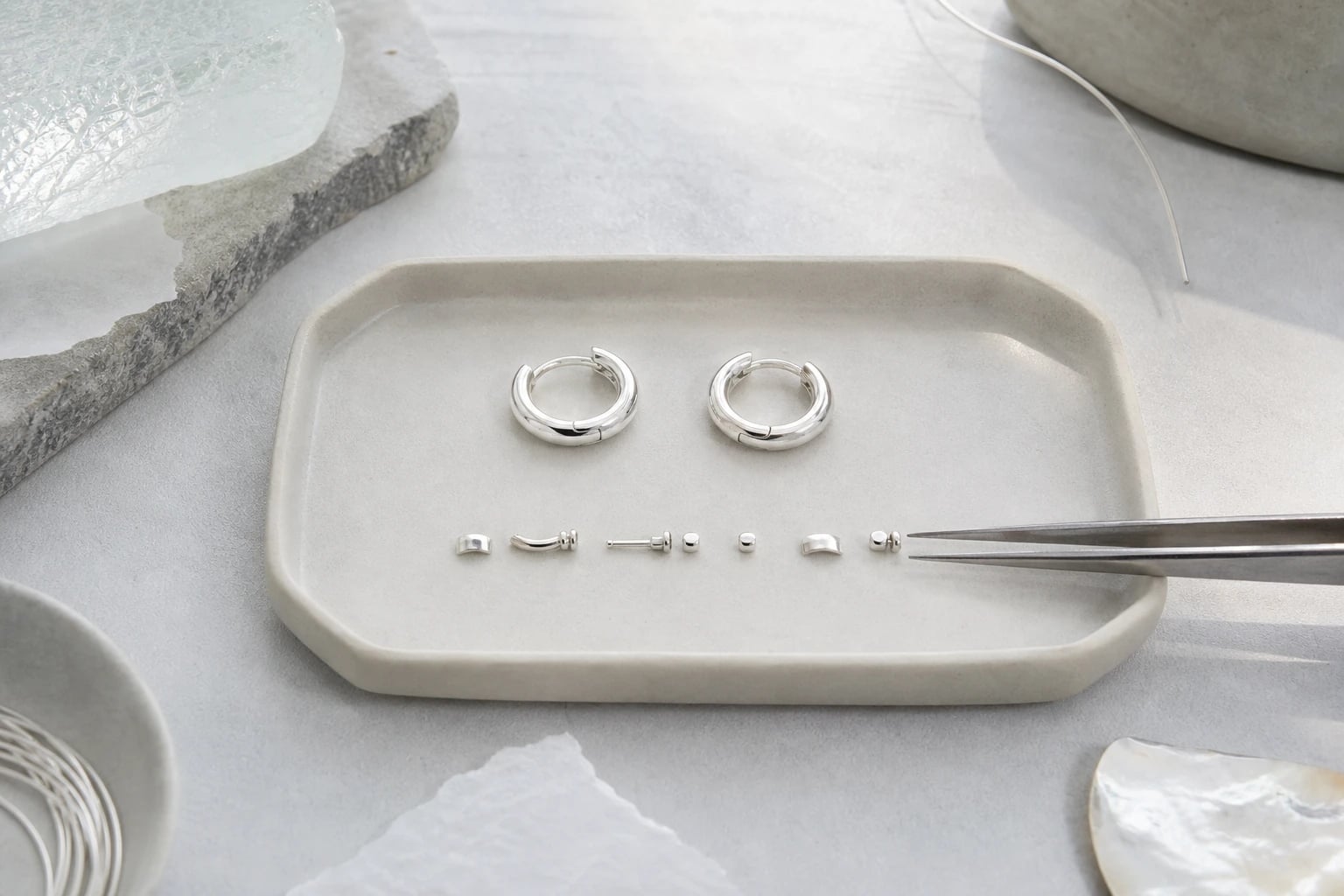Pair of silver huggie hoops with tiny hinge components in a row on a pale ceramic tray