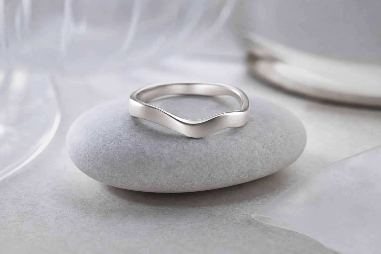 Satin silver wave band resting on a smooth pale pebble