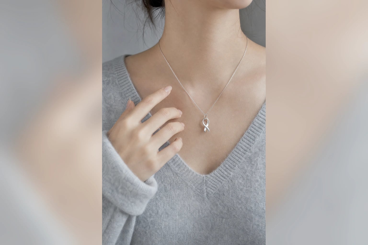 Silver ribbon pendant necklace worn at the neckline of a soft gray knit