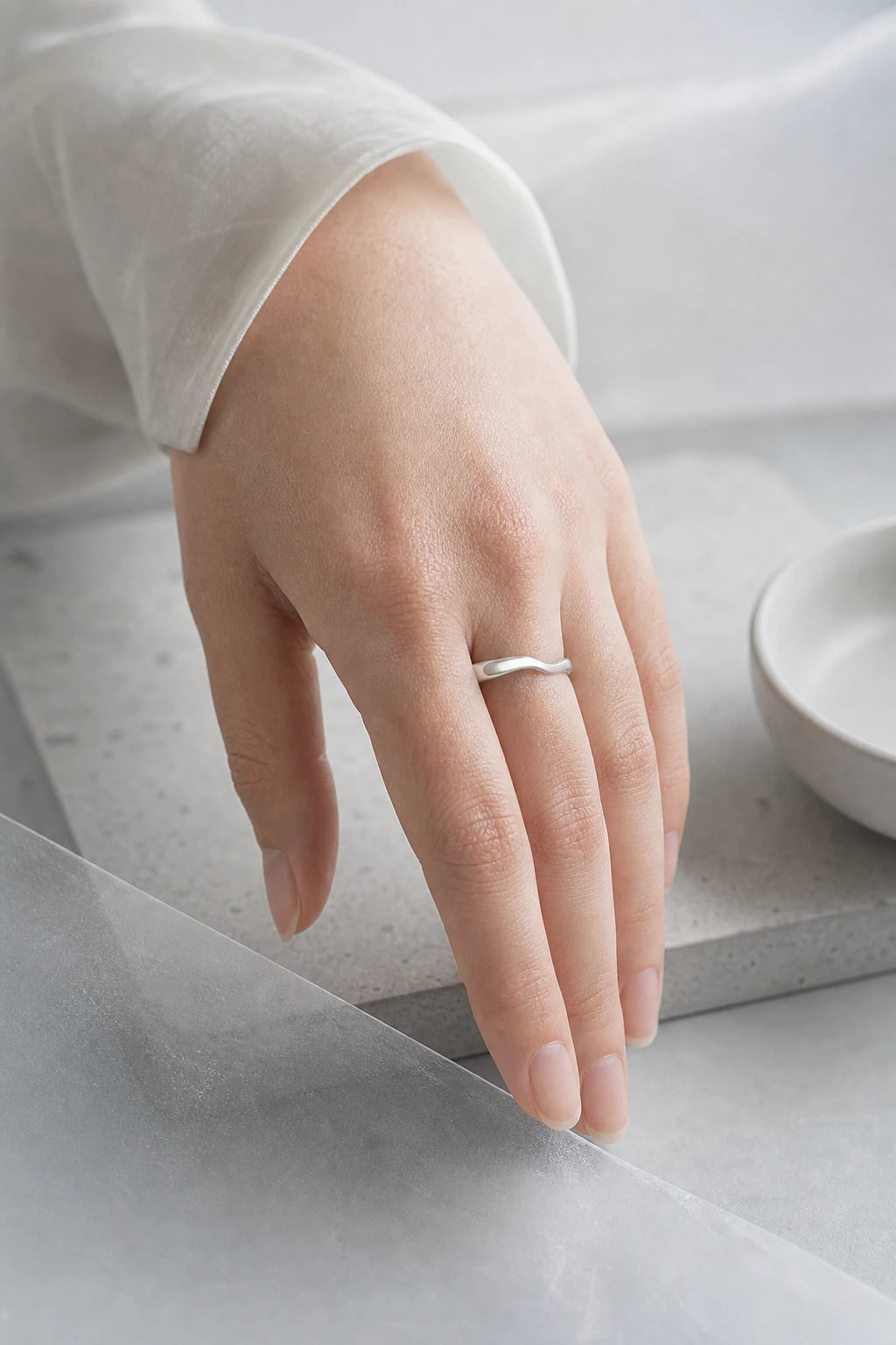 Hand resting on a pale concrete ledge wearing a slim silver wave band