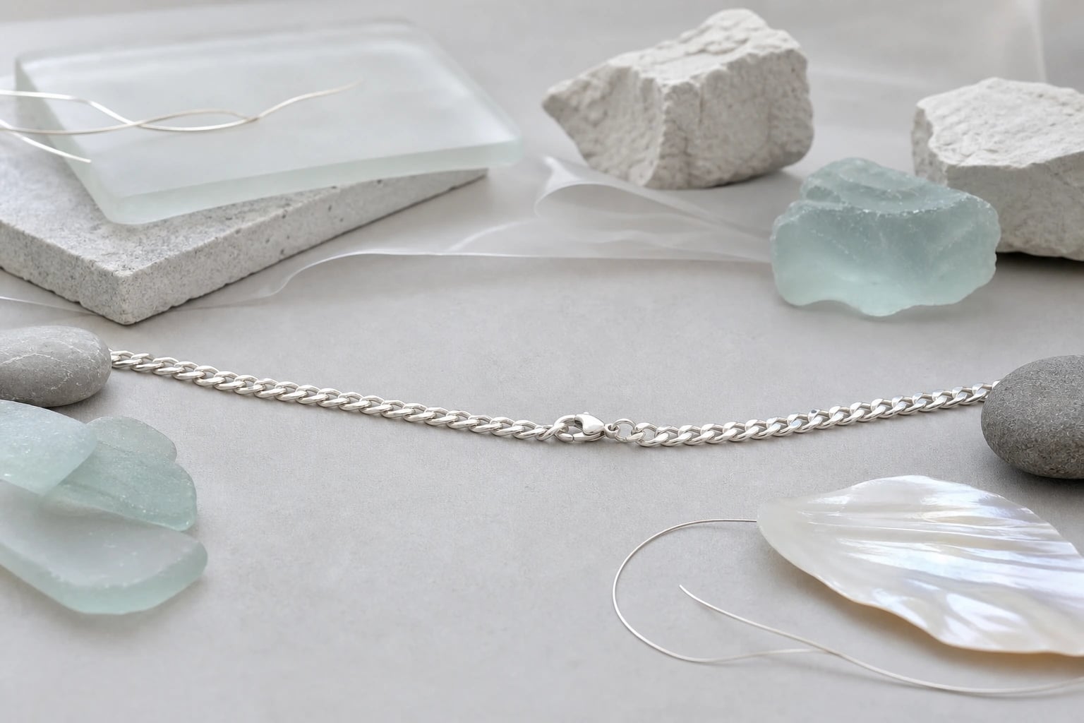 Wide still life with a silver curb chain resting as a calm line among sea glass and stone