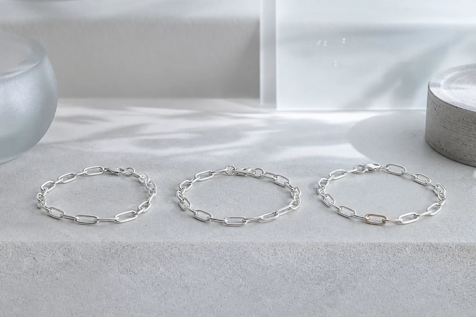 Three silver chain bracelets in a row on a pale showroom ledge