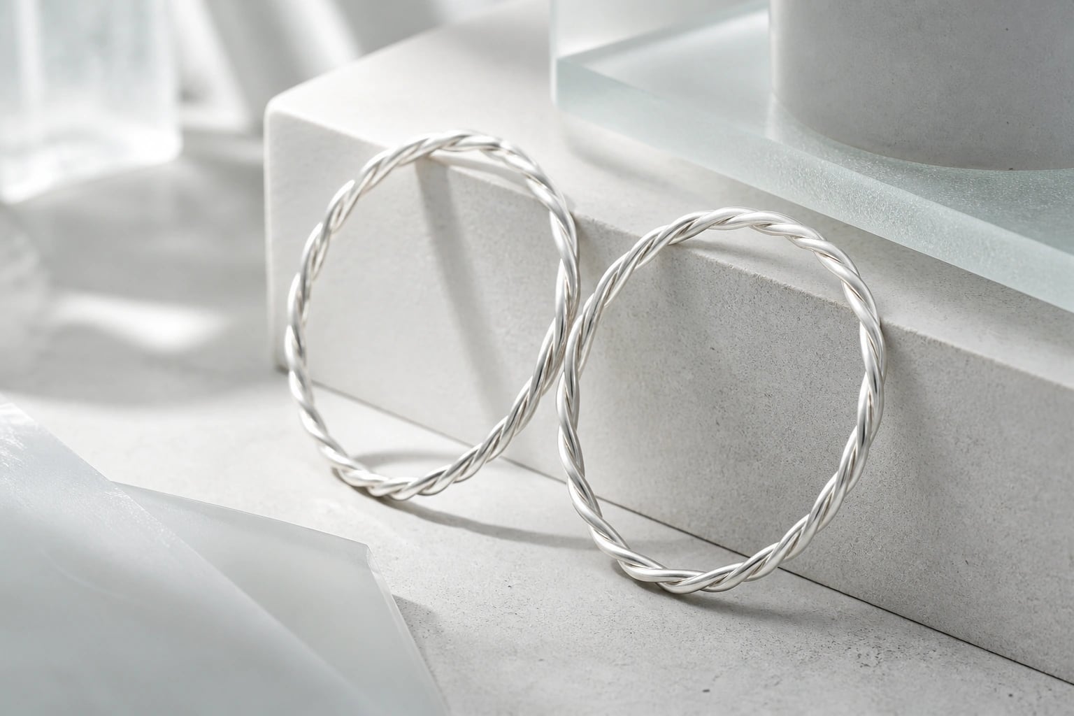 Two twisted silver bangles leaning on a pale showroom ledge