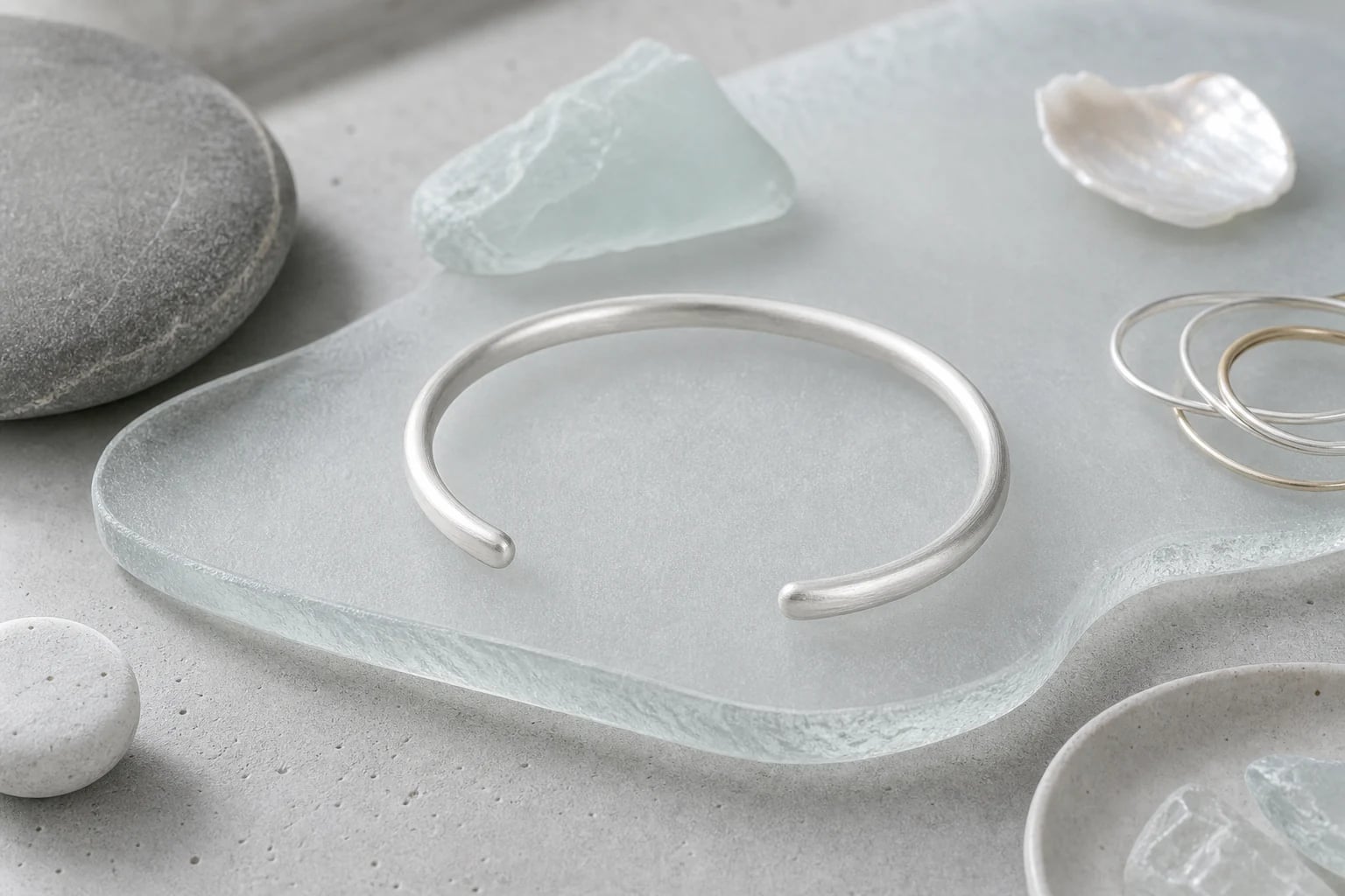 Satin silver open cuff resting on a frosted glass slab