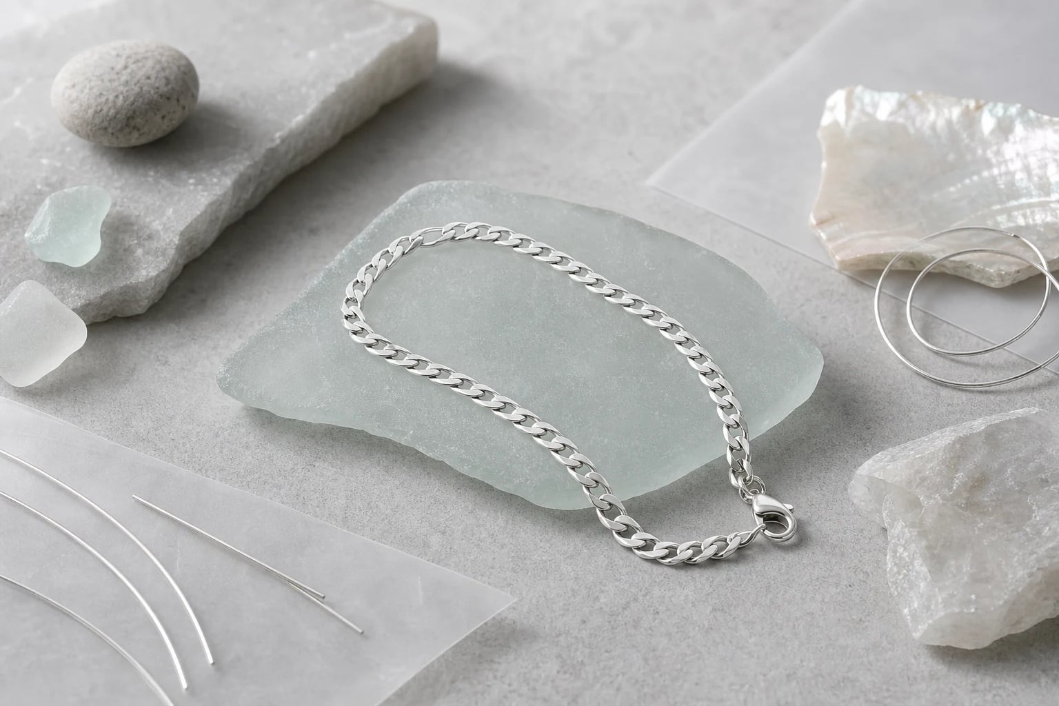 Silver curb chain bracelet draped across pale sea glass