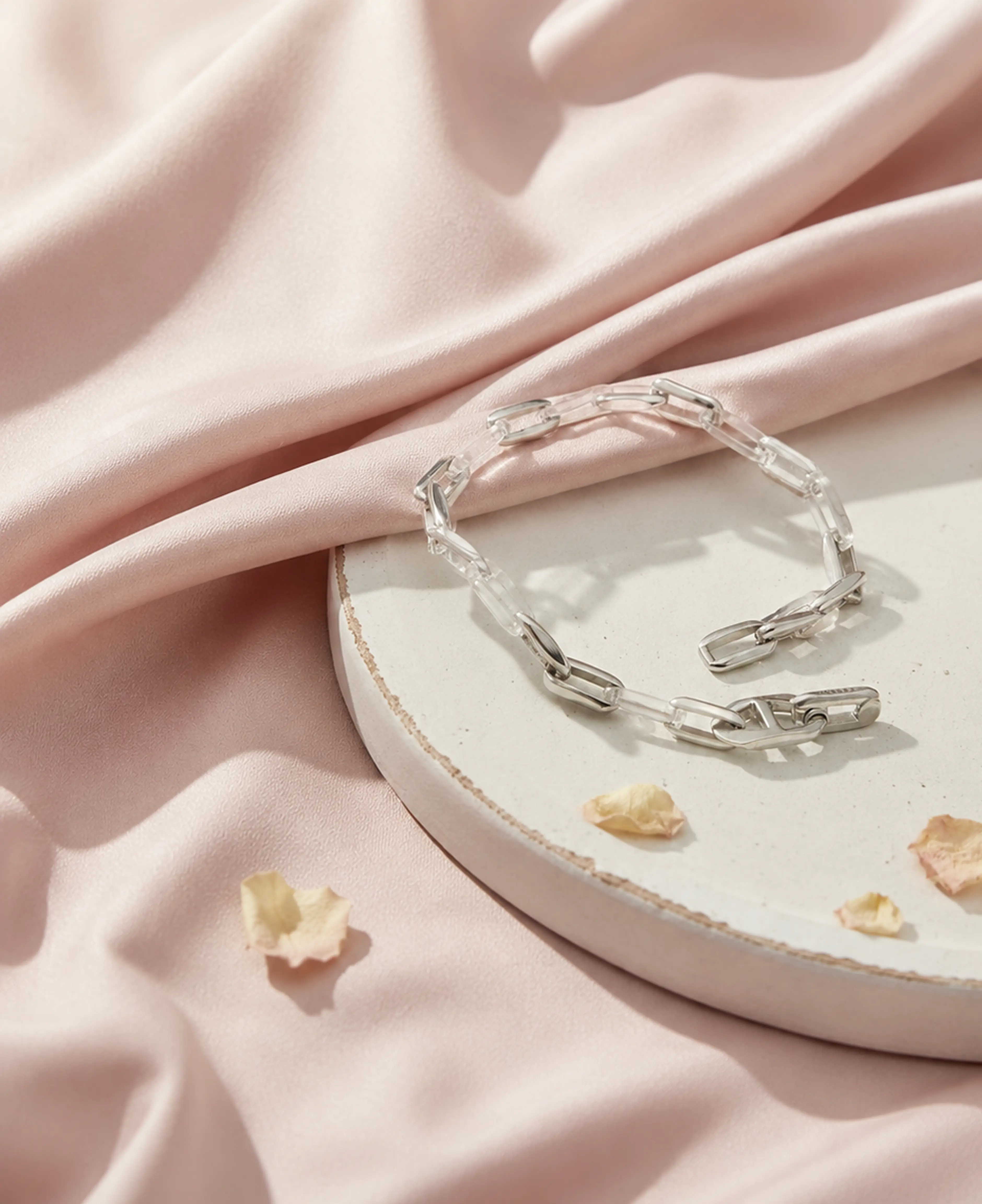 Silver link bracelet arranged on blush fabric and a ceramic plate